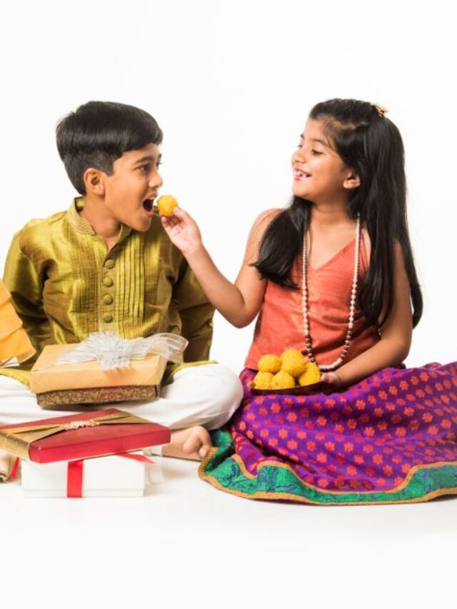3 indian kids or siblings in traditional wear sitting on sofa or white background, holding gifts and sweets or laddu